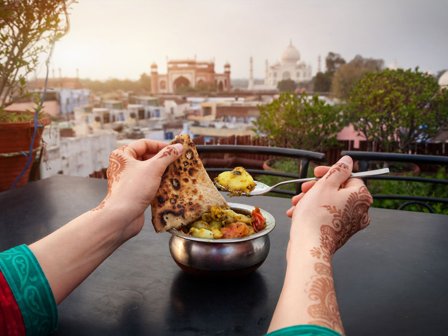 Woman eating traditional Indian food in rooftop restaurant with Taj Mahal view in Agra, Uttar Pradesh, India