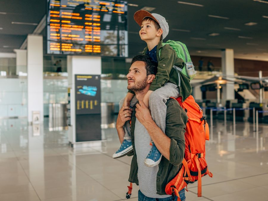 A man carrying a child on his shoulders while walking in the airport.