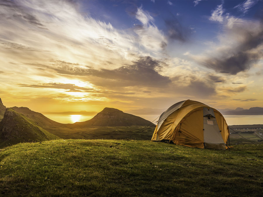 Yellow tent on a mountain with sunrise on the background