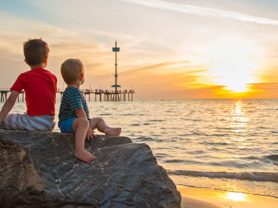 Two boys sitting on a rock looking at the sunset on the beach